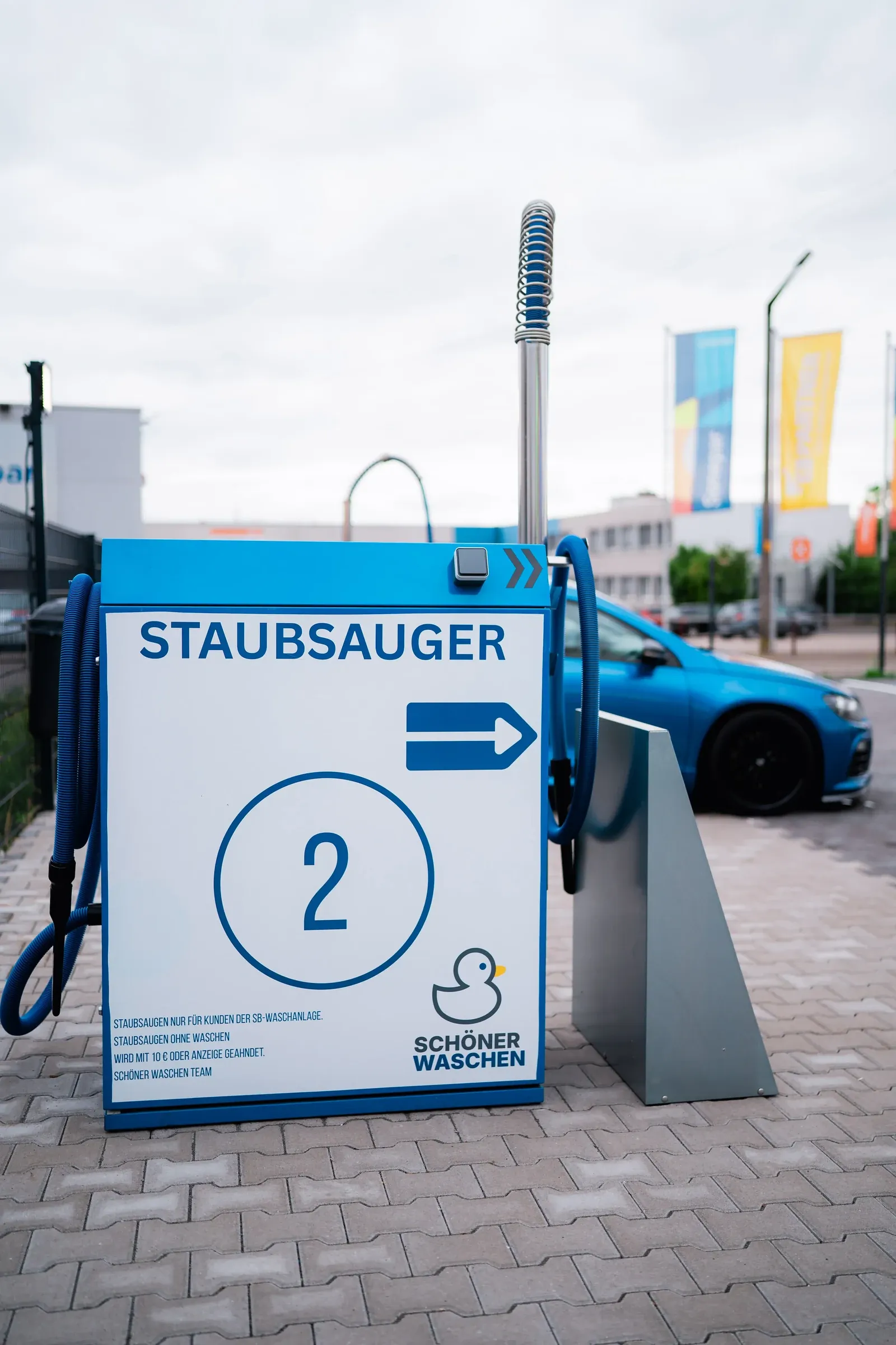 Blaues Hinweisschild „Staubsauger“ mit Pfeil und Stationsnummer auf dem Gelände